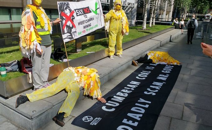 Activists dressed as coal mine canaries outside government offices. A couple of them hold up banners,whilst two more lie 'dead' on the pavement